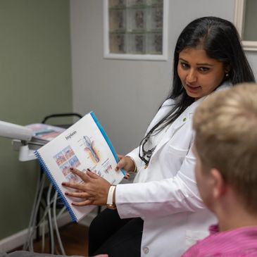 Dr. Gundarpi showing a patient a dental textbook while explaining treatment