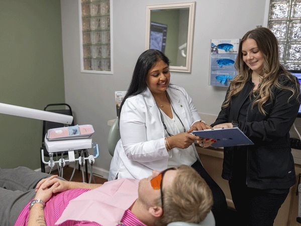 Dr. Gundarpi working with staff member to help a patient sitting in treatment chair