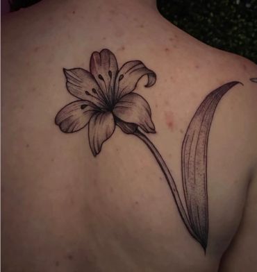 Black ink lily flower tattoo on upper back.