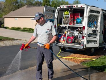 Man using a hose to spray water near a work van.
