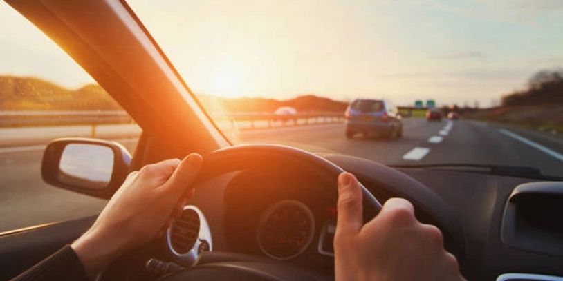 Person driving a car on a highway during sunset.