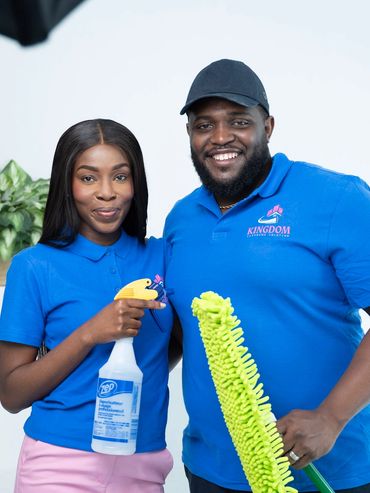 Two smiling cleaners in blue uniforms holding cleaning tools.