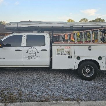White service truck with ladders on top parked on gravel.