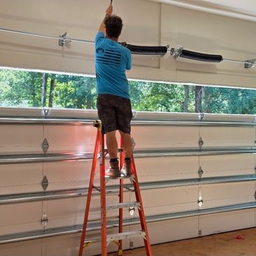 Man fixing a garage door spring while standing on a ladder.