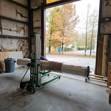 Large cylindrical object on a green dolly inside a warehouse with an open door showing fall trees.