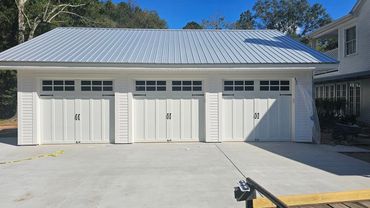 A newly built three-car white garage with a metal roof on a sunny day.