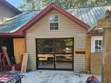 Newly installed modern glass garage door on beige house under construction.