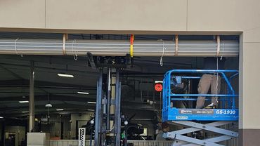 Worker on a blue scissor lift and a forklift inside a garage or workshop.