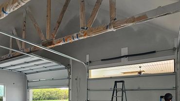 Person working on garage door installation in an unfinished garage.
