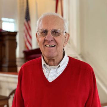 Elderly man in red sweater smiling indoors.