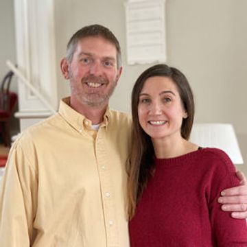Smiling couple posing indoors, man in yellow shirt, woman in red sweater.