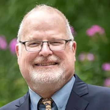 Smiling man with glasses and beard in a suit.