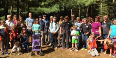 Group of diverse people posing outdoors with dogs and a stroller.