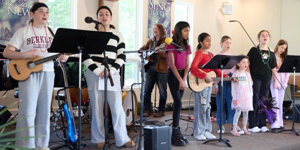 Group of young musicians and singers performing indoors with instruments and microphones.