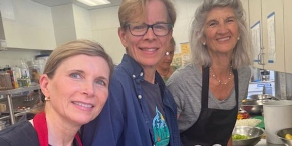 Three women smiling together in a kitchen setting.