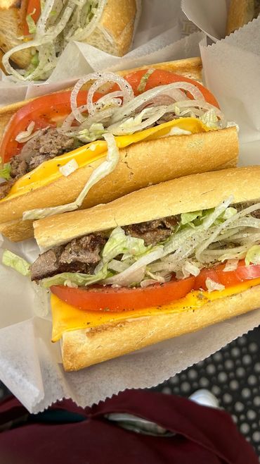 Four delicious cheesesteak sandwiches with lettuce, tomato, and onions.