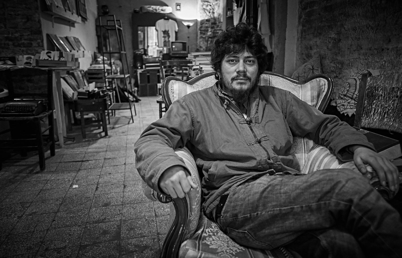 black and white photo of a gypsy sat in a chair in his shop.