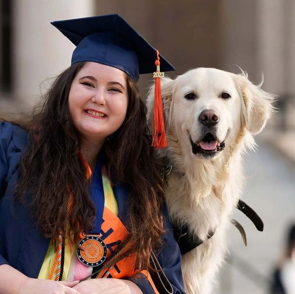 A smiling white female wearing graduation attire with her service dog.