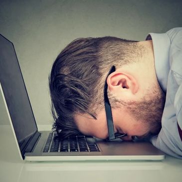 Man frustrated with laptop, resting head on keyboard.