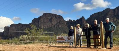 Five people standing by a gate with rocky mountains in the background.