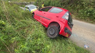 Red car crashed off road with police officers nearby.