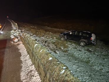 Car crash off a stone wall at night with snow.
