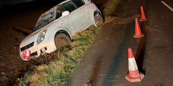 White car crashed off road at night with cones on road.
