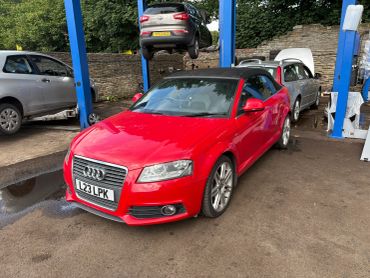 Red Audi convertible at a car repair shop with other vehicles.