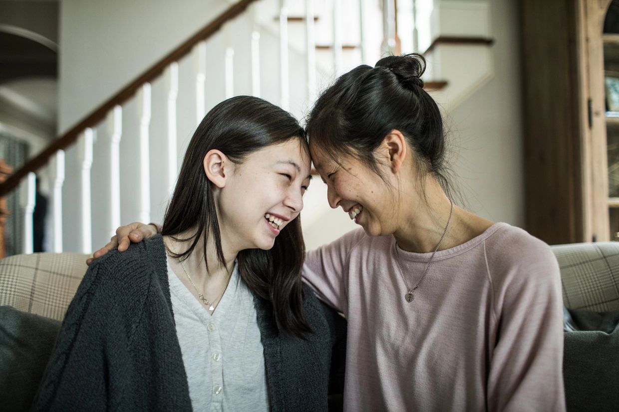 A mother and daughter smiling and hugging each other while sitting on a couch.