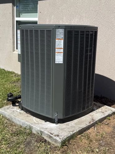 Outdoor air conditioning unit installed on a concrete slab beside a house.