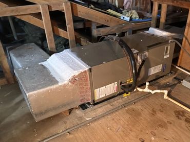 A HVAC unit installed in an attic space with exposed wooden beams and piping.