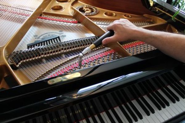 Man tuning a grand piano with a tuning hammer and a gang mute.