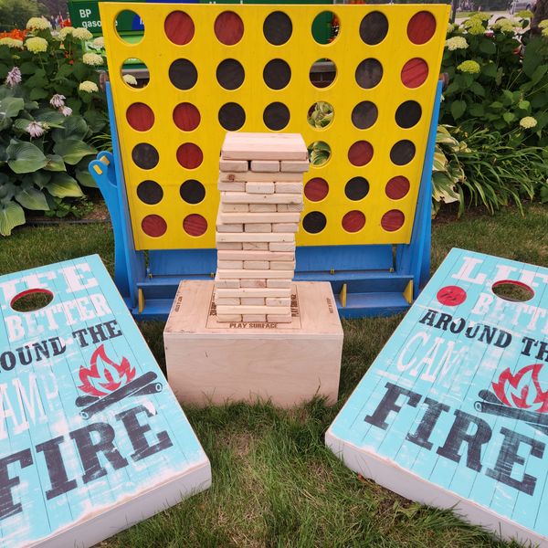 Outdoor games including giant Connect Four, Jenga, and cornhole on grass.