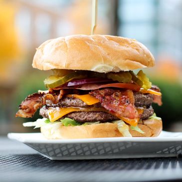 Double cheeseburger with bacon, pickles, and lettuce on a white plate.