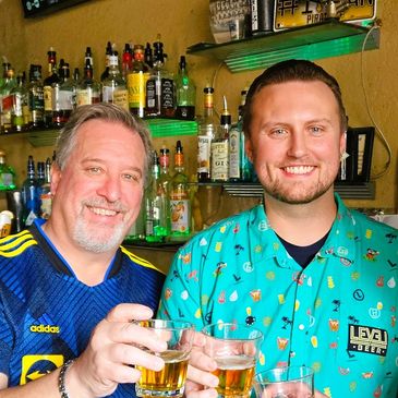 Three men smiling and toasting drinks at a bar with sports décor.