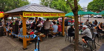 Outdoor gathering under a pavilion with local brews and people enjoying food and drinks.