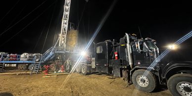 Heavy truck beside an oilfield rig at night, with third-party truck logos covered.
