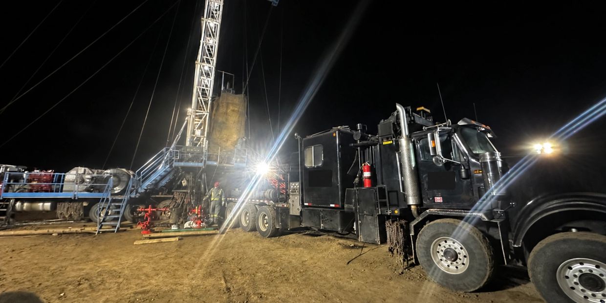 Oilfield service truck and rig at a night work site.
