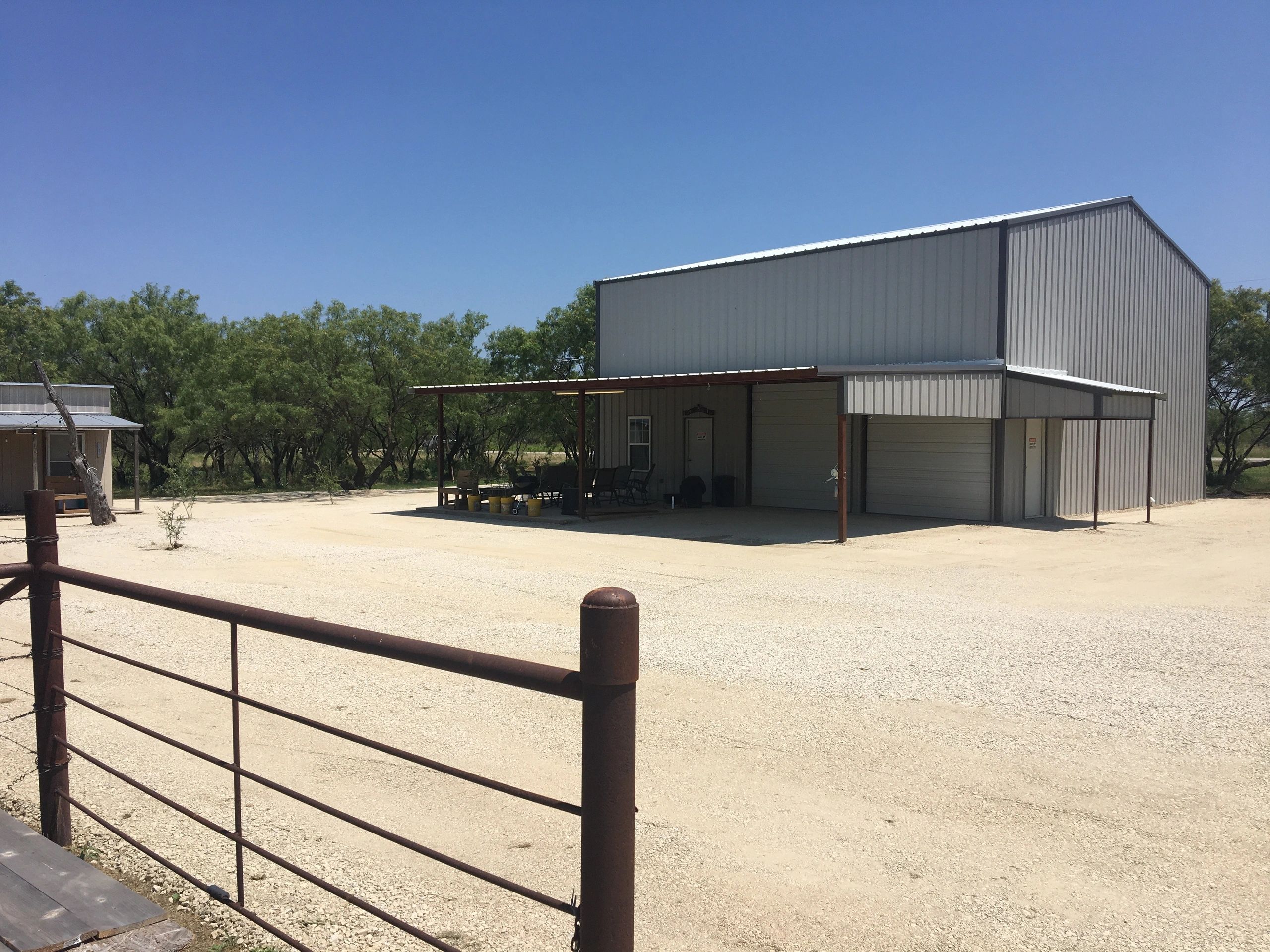 A metal building with a covered porch in a rural area under a clear blue sky.