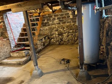 Old basement with stone walls, wooden beams, and a water heater.