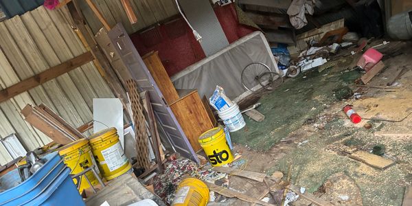 Cluttered shed filled with old furniture, buckets, and debris scattered on the floor.