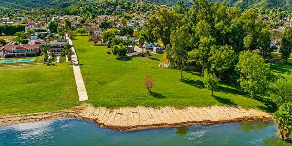 A lakeside park with green grass and trees near a neighborhood.