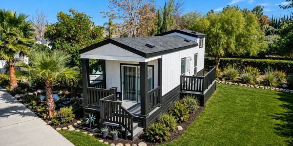 A modern tiny house with a porch in a lush garden.