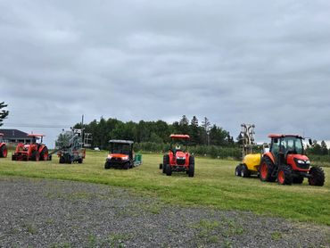Several orange tractors and farm equipment lined up on a grassy field under a cloudy sky.