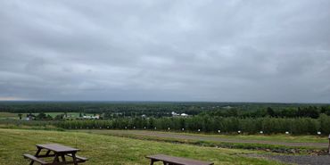 Picnic tables overlook a vast, green agricultural landscape under a cloudy sky.