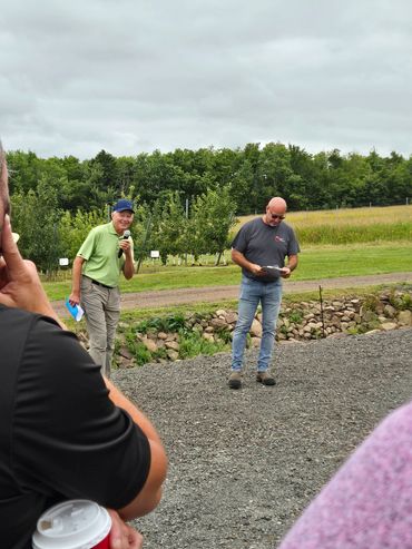 Two men speaking outdoors with a small audience during a cloudy day.