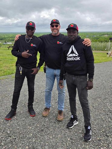 Three men posing outdoors on a cloudy day with matching hats and black tops.