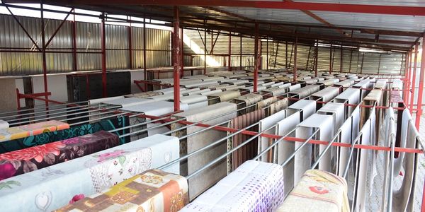 Gemini şunu dedi:
2000 m2 gibi geniş ölçekli bir halı yıkama fabrikasında, yıkama işlemi kadar kritik olan aşama kurutmadır. Bu kapasitedeki bir tesiste manuel yöntemler yetersiz kalacağı için Raylı Otomatik Askı Sistemi (Konveyör Kurutma) devreye girer.
İşte bu sistemin teknik işleyişi ve profesyonel detayları:
1. Sistemin Yapısı ve Mekanik Bileşenleri
Büyük bir tesiste kurutma alanı, fabrikadan bağımsız bir bölme veya özel yalıtımlı bir oda olarak tasarlanır.
Raylı Taşıyıcı Hat: Tavan yüksekliğine monte edilen, halıların yıkama makinesinden çıktıktan sonra asıldığı paslanmaz çelik hatlardır.
Halı Asma Aparatları (Kıskaçlar): Halının ağırlığını taşıyabilecek güçte, dokuya zarar vermeyen ve kaymayı önleyen özel kilit sistemleridir.
Motorlu Zincir Sistemi: 2000 m2'lik bir alanda halıların elle taşınması imkansızdır; bu yüzden sistem bir motor yardımıyla halıları kurutma tüneline otomatik sürer.
2. Kurutma Odası Dinamiği (İklimlendirme)
Sadece asmak yeterli değildir; 2000 m2 kapasiteli bir işletmede "Hızlı Devir" (Fast Turnover) esastır.
Nem Alma Cihazları (Industrial Dehumidifiers): Ortamdaki nemi yoğuşturarak dışarı atar. Halının içindeki nem %5'in altına düşene kadar çalışır.
Sıcak Hava Üreteçleri: Genellikle doğalgazlı veya elektrikli ısıtıcılar kullanılır. İdeal kurutma ısısı halının dokusuna zarar vermemesi için 40°C - 50°C arasında sabitlenir.
Hava Sirkülasyon Fanları: Sıcak havanın halıların arasında "S" çizerek dolaşmasını sağlar. Bu, halının alt ve üst kısmının aynı anda kurumasını sağlar.