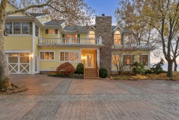 Yellow two-story house with stone chimney and autumn trees.