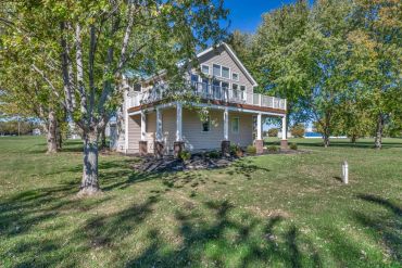 House with a large porch surrounded by trees and grass.
